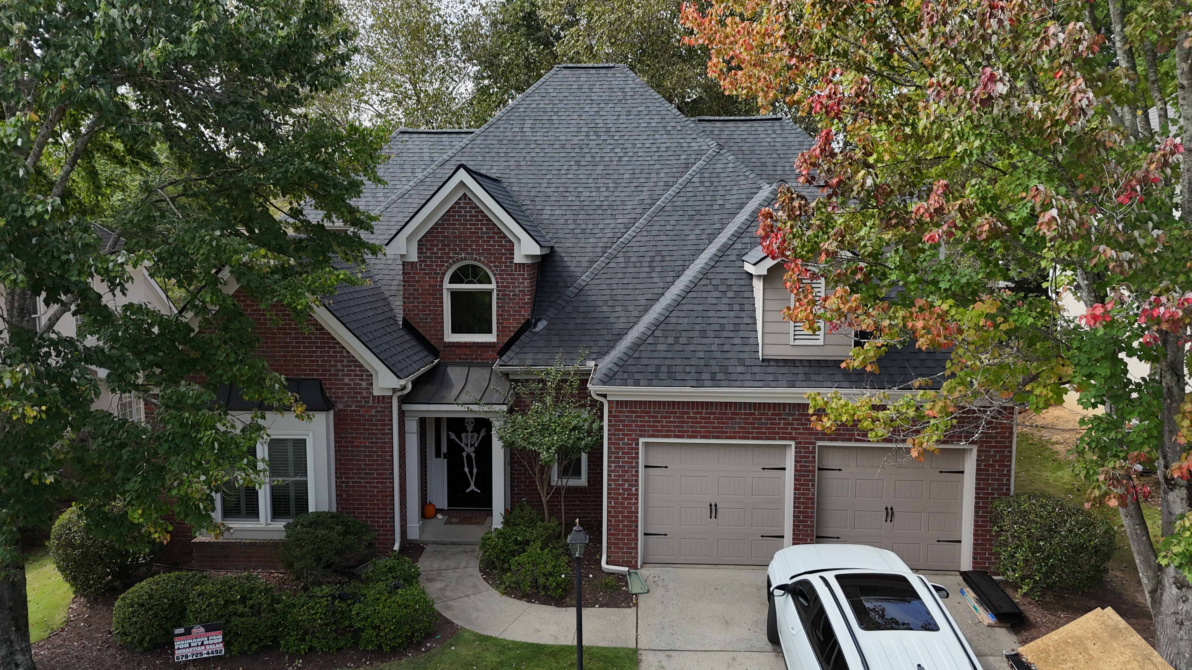 Completed dark shingle roof on red brick home — aerial view